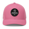 Pink trucker cap with mesh back and black circular patch featuring a dog logo and 'Franklin Brown' text, adjustable snapback closure